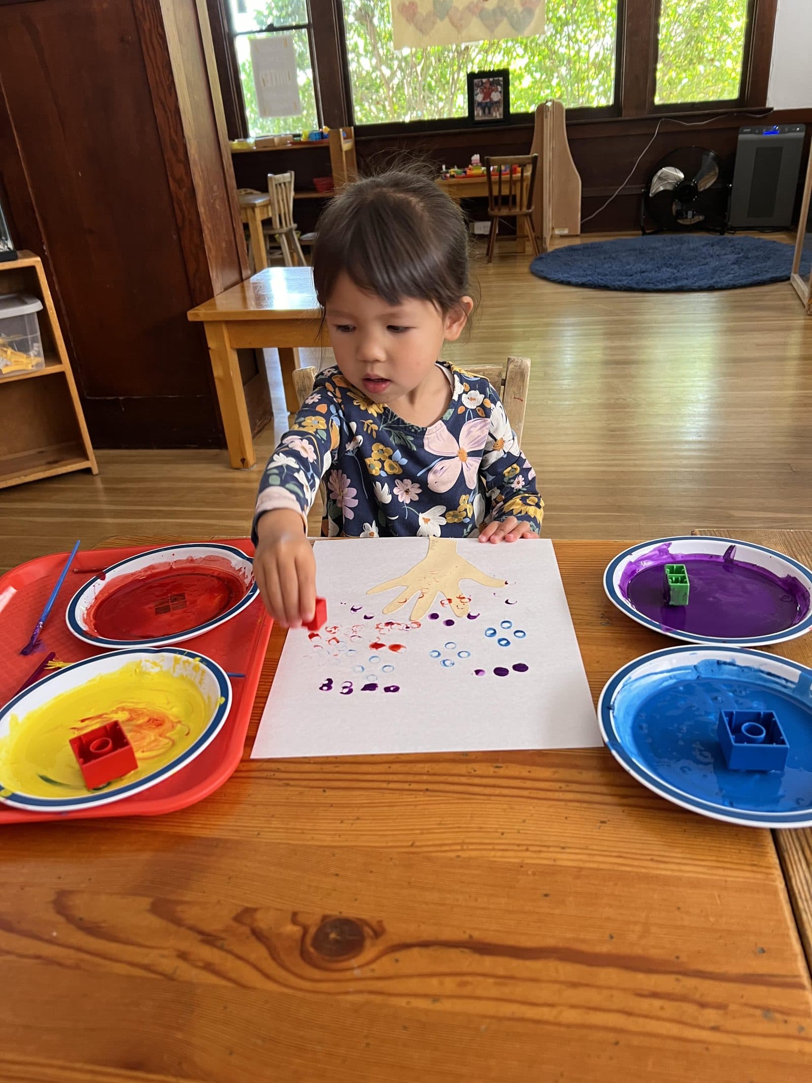 A young student painting a hand-print at The Child Unique Montessori Schools